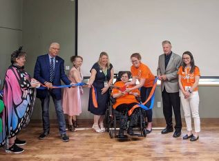 Nurse Practitioner, Rebecca Mckeowen helps a resident of Fairmount Home cut a ribbon to symbolize the launch of Fairmount Home’s BPSO pre-designation with Deputy Warden, Ron Vandewal, MPP John Jordan and other Fairmount Home staff.